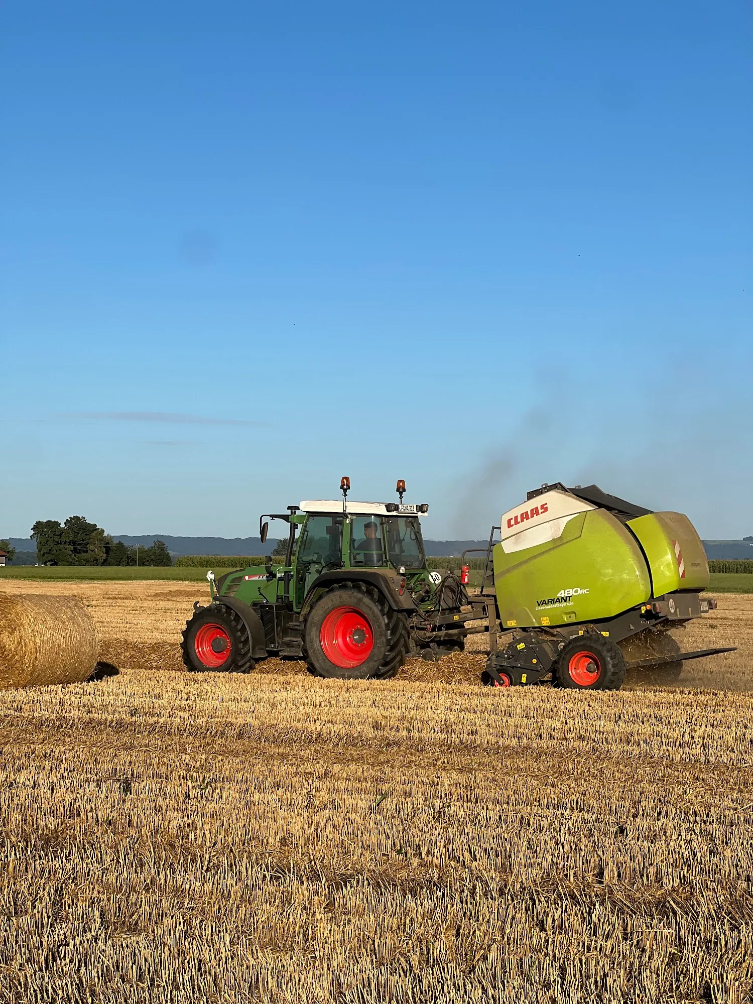 Fendt Traktor und Claas Variant 480 Rundballenpresse bei der Strohernte auf dem Stoppelfeld
